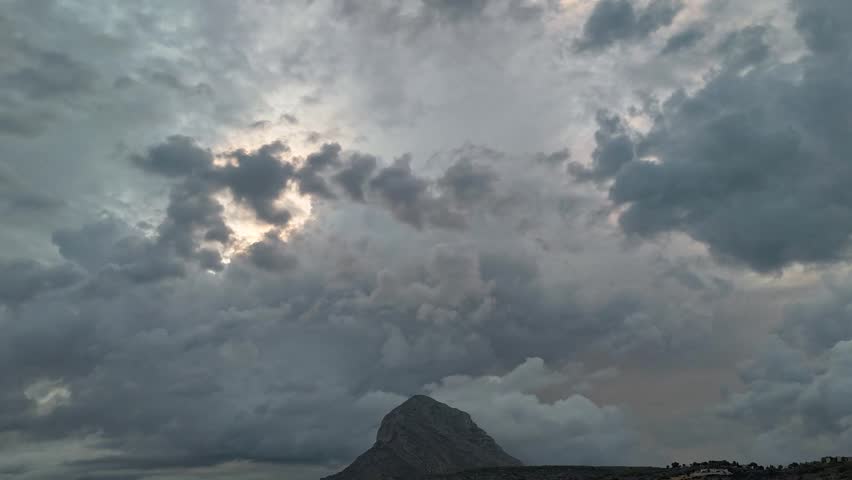 Hyperlapse aerial drone footage of storm clouds over Javea, Costa Blanca, Spain, at dusk, with the Montgo mountain silhouette and town lights below