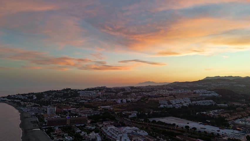 Hyperlapse aerial drone footage of a sunset over La Cala de Mijas, Costa del Sol, Spain, with pink and orange clouds, a sandy beach, and coastal town lights