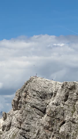 People standing on a high mountain summit with a cross, as birds fly around and clouds pass