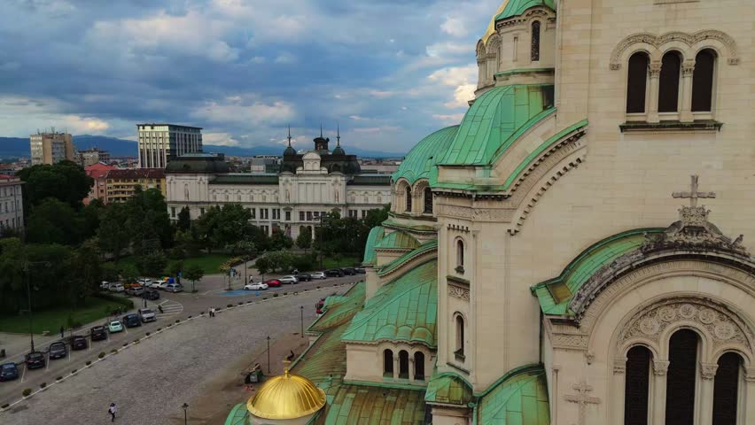 Low angle drone shot framing the golden domes of the Alexander Nevsky Cathedral in Sofia, Bulgaria. Historic Orthodox christian landmark architecture under bright daylight