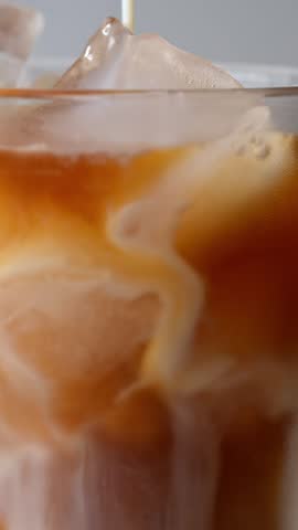 Macro close-up of ice latte with milk pouring creating abstract pattern

