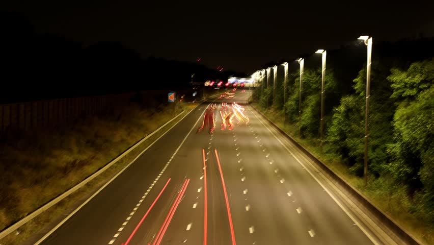 Time-Lapse Shot of Traffic Light Trails on a British Motorway at Night, Showing Illuminated Overhead Gantry Signs Directing Traffic to Heathrow Airport, Gatwick Airport, and the M4