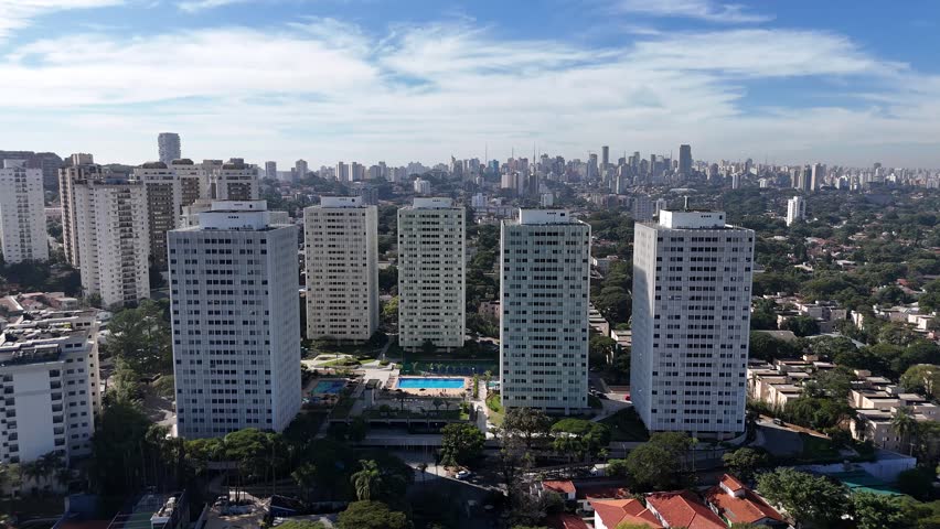 Cinematic forward drone flight over a dense skyline of high-rise buildings on a sunny day with a clear blue sky in an upscale district of São Paulo, Brazil. Urban cityscape aerial footage