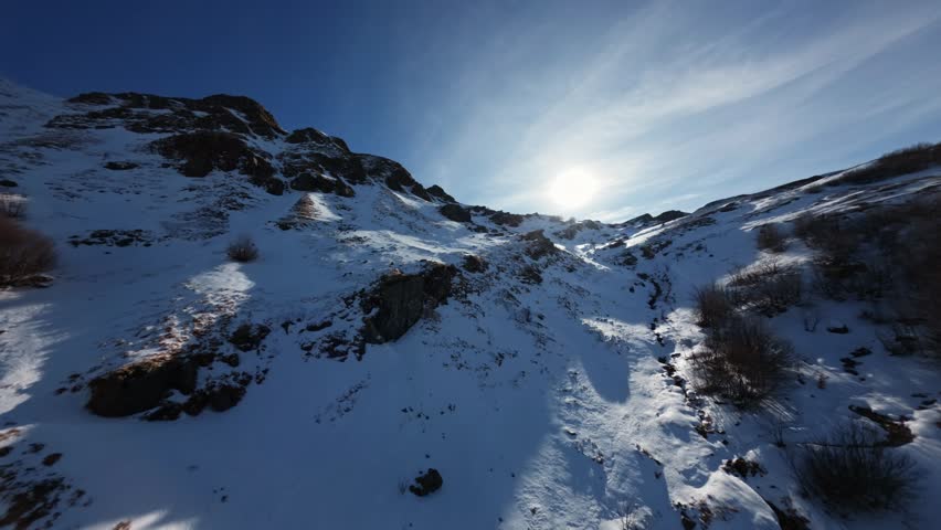 A highspeed cinematic drone flight maneuvers over a rugged snowcovered mountain ridge to reveal a frozen alpine lake Lago Scuro under a bright blue winter sky.