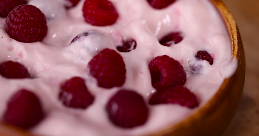 Pink yogurt with red raspberries, a cup of yogurt and fresh raspberries on a black textured countertop