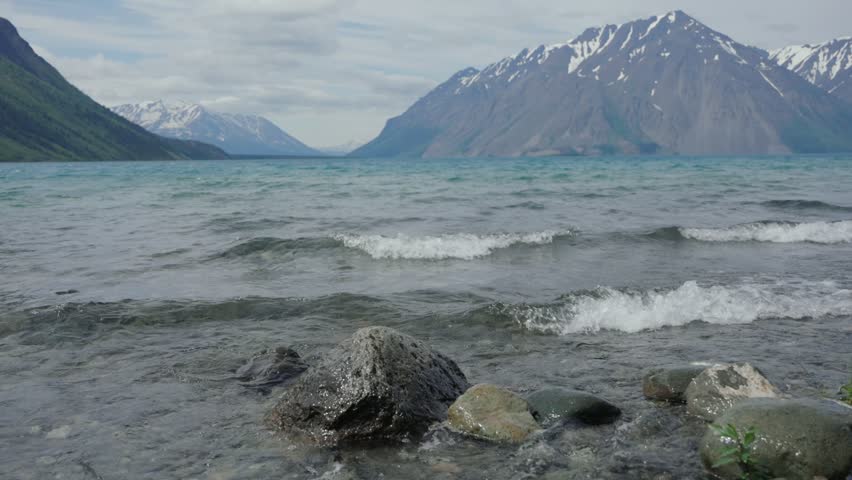 Kathleen Lake waves washing over shoreline rocks with snow capped mountains in the background