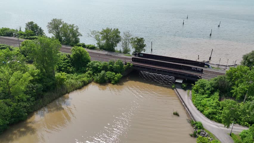 Railroad tracks cross the port of a river by means of bridge as the muddy water emulsifies with the lake.