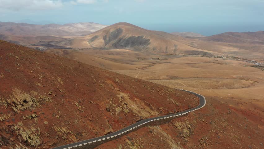 Drone view of the FV-30 winding road crossing the volcanic mountains of Risco de Penas in Fuerteventura, Canary Islands. Scenic curves and dramatic natural landscape.