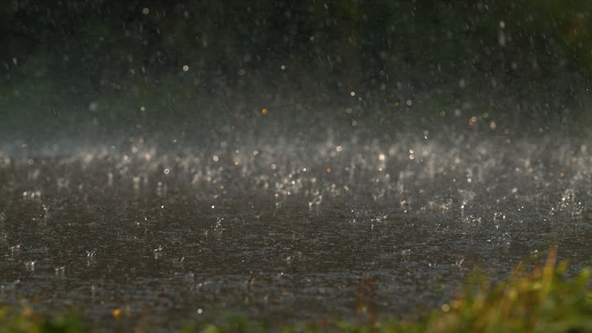 Close-up longboard wheels and feet splashing through rain on wet pavement in ultra slow motion.