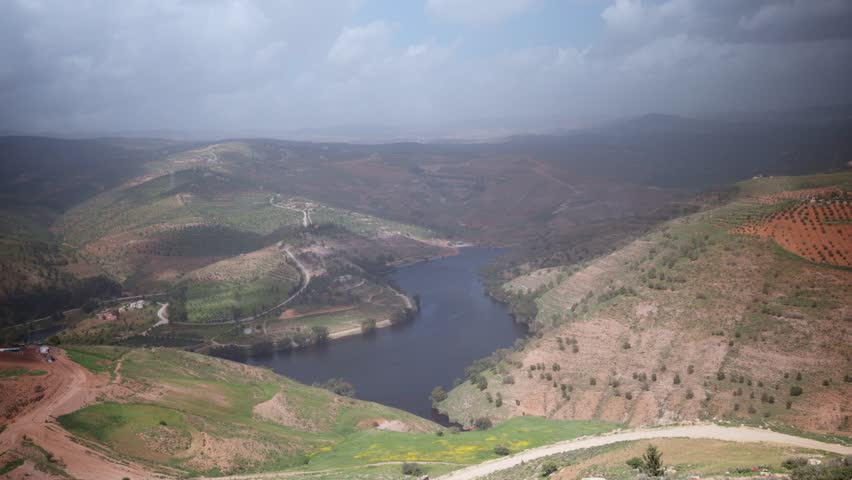 Aerial view of King Talal Dam full of water during spring in Jordan
Aerial drone footage of King Talal Dam in northern Jordan during spring, with the reservoir at a high water level after seasonal rainfall. The scene features lush green hills, agricultural landscapes, dramatic cloudy skies, and one of Jordan’s most important freshwater reservoirs, highlighting the country’s natural beauty and water resources.