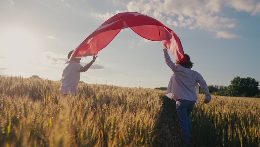 Happy little boys run through golden wheat field waving Turkish national flag during sunset. Warm evening light, agricultural landscape and patriotic spirit celebrate heritage, rural traditions.Turkey