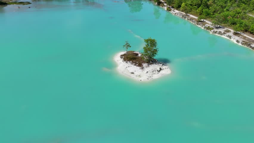 Aerial view of a small island with trees in the middle of a vibrant turquoise lake in Beruntung Baru, South Kalimantan, Indonesia.