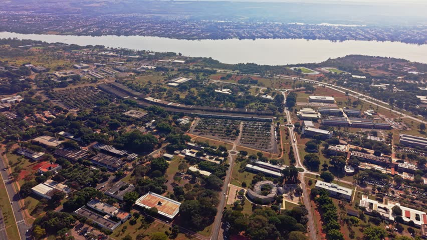 Wide aerial drone shot of the expansive University of Brasília (UnB) campus, featuring the long ICC building, surrounding nature, and Paranoá Lake