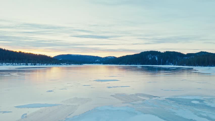 Frozen Lake With Snow-covered Mountain And Forest In The Background At Sunrise. - aerial shot