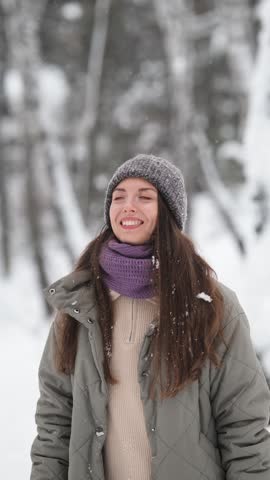A beautiful young woman in winter clothes is happily spending her free time in a snowy forest. She enjoys the first snow. Active winter recreation.