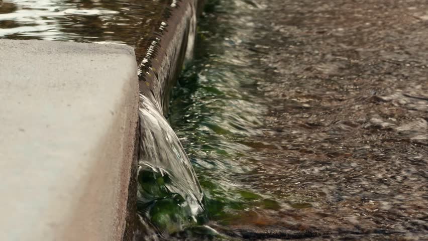 Water spills over a concrete ledge into a rocky streambed below