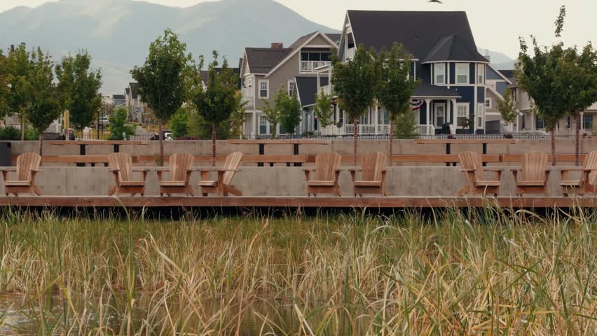 Rows of wooden chairs sit along a boardwalk facing marsh grass and homes