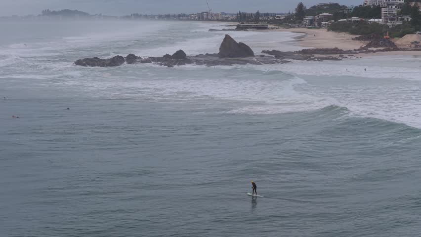 Surfers Riding Waves Near Large Coastline Rocks At Currumbin Beach – Wide Aerial Shot