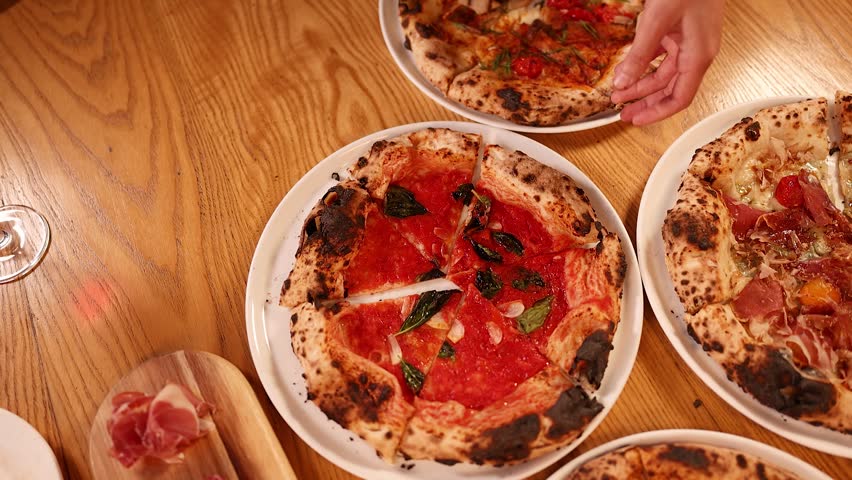 Overhead view of people sharing various Neapolitan pizzas and cured meats at a restaurant.