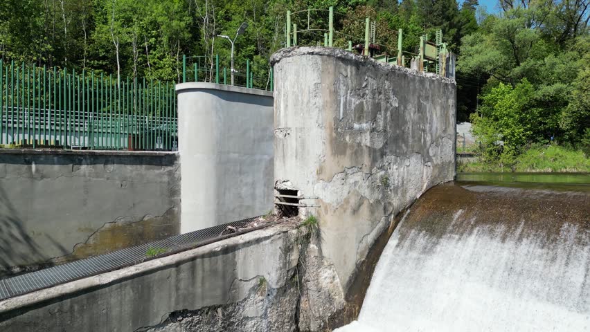 Aerial summer landscape showing the Koszarawa River, water flowing over a weir, hydrotechnical structures, rocky shore, lush vegetation and tranquil natural surroundings of polish land.