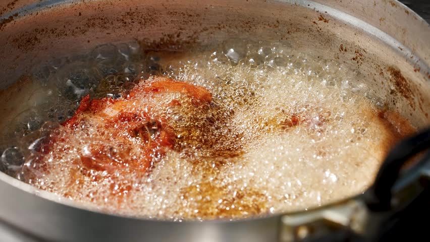 Extreme close-up of seasoned chicken deep frying in bubbling hot oil within a metal wok.