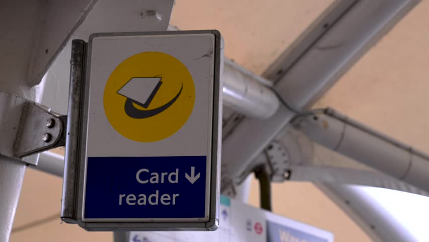 Static close-up of a contactless card reader sign hanging from metal beams at a public transport station.