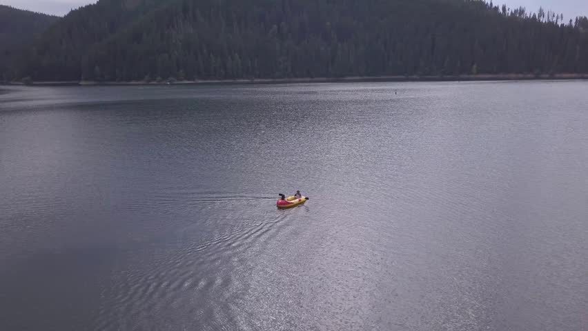 A red inflatable boat carries two people as they paddle across a tranquil lake surrounded by forested hills. Ideal for outdoor adventure themes or travel content.