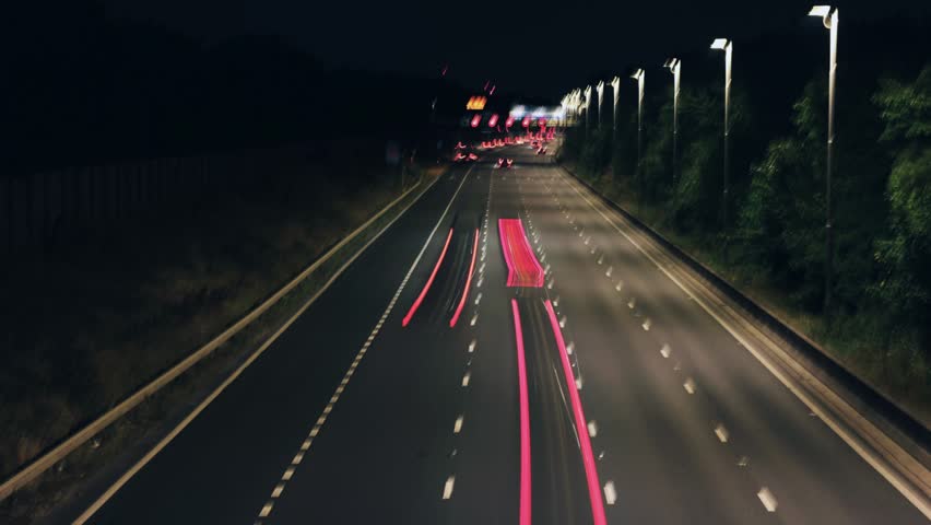 A Time-Lapse Shot of Traffic Light Trails on a British Motorway at Night, Showing Illuminated Overhead Gantry Signs Directing Traffic to Heathrow Airport, Gatwick Airport, and the M4
