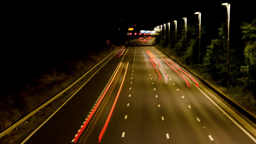 A Time-Lapse Shot of Traffic Light Trails on a British Motorway at Night, Showing Illuminated Overhead Gantry Signs Directing Traffic to Heathrow Airport, Gatwick Airport, and the M4