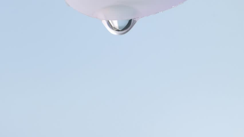 A transparent drop of serum slowly flows down, macro, blue background.