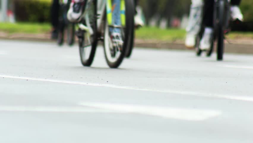 Close up view of bicycle wheels and legs of many cyclists participating in bike ride event. Ground level perspective highlights speed and motion on smooth road surface with blurred green background.