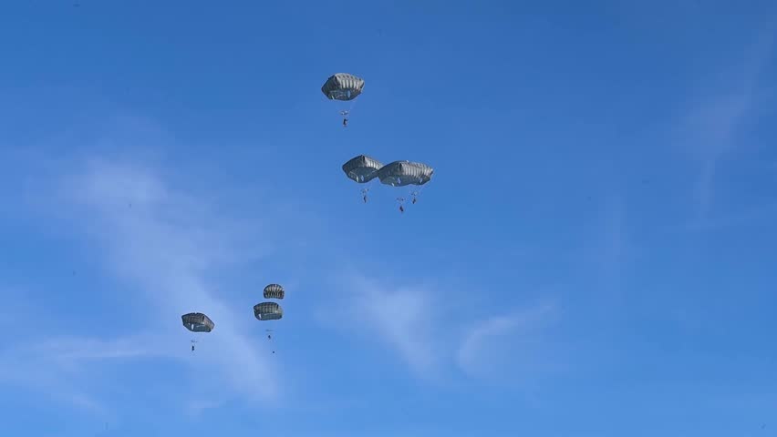 Military Paratroopers Descending Beneath Parachutes Against Clear Blue Sky During Precision Airborne Training Exercise Mission.