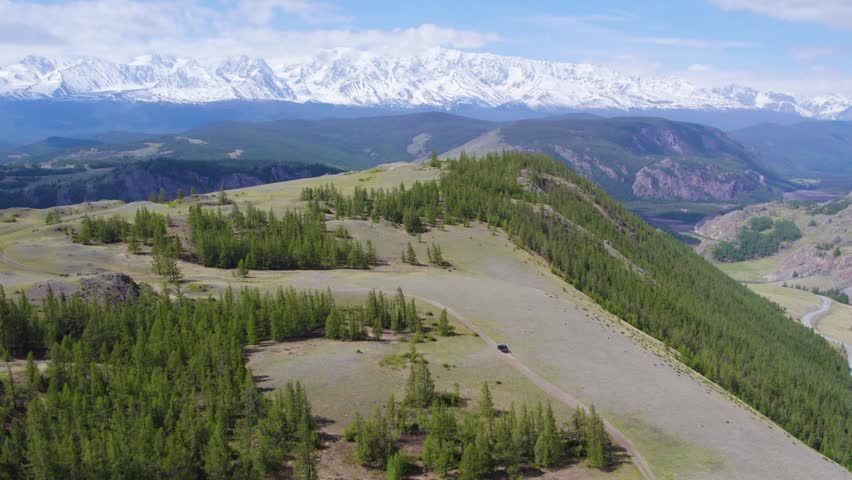 Offroad vehicle on winding mountain ridge road with snow-capped peaks on horizon