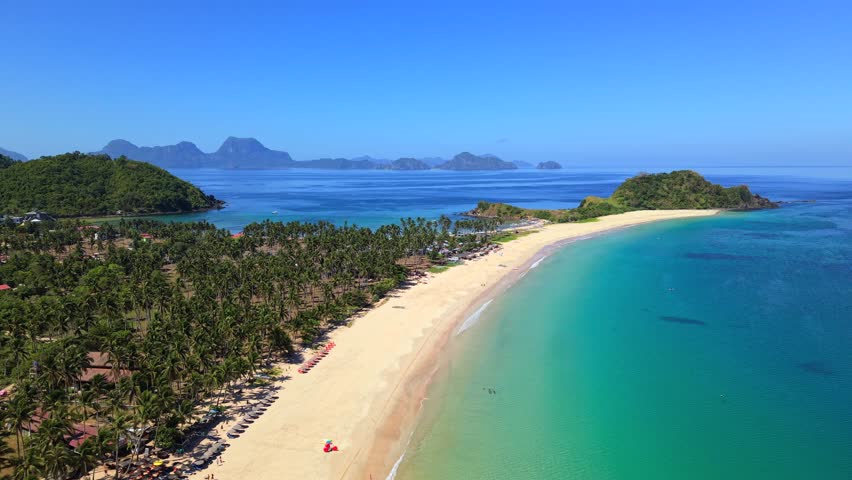 Cinematic aerial view of Nacpan Beach in El Nido, Palawan, Philippines with crystal clear water, palm trees and distant tropical islands. Exotic paradise coastline.