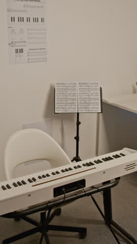 Vertical shot of digital piano standing in empty classroom with sheet music on stand. Footage for promoting online music lessons, piano schools, or educational courses