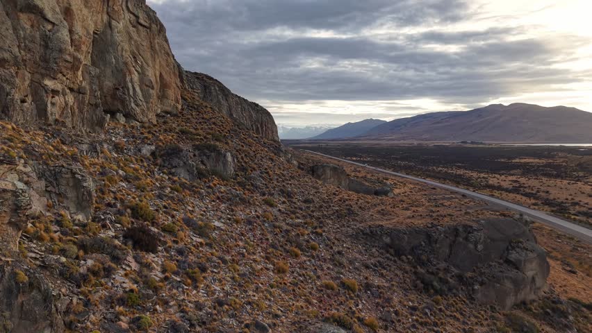 Scenic landscape of Patagonia in Argentina with rocky cliffs and a long road stretching through the vast steppe under a cloudy sky