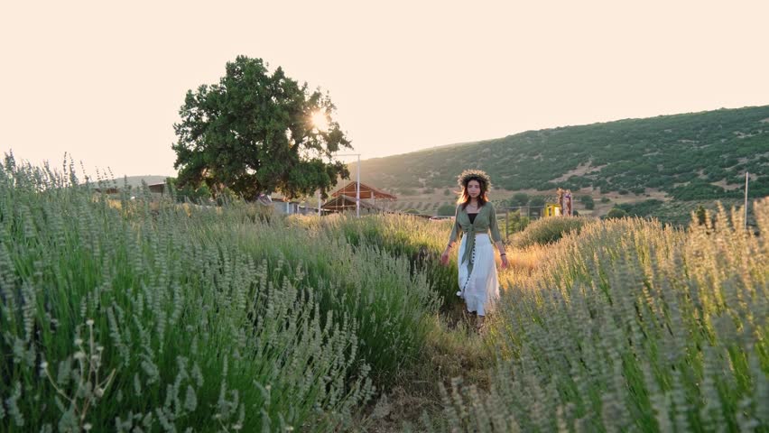A young woman wearing a flower crown walks through a lavender garden; sunset light, mountain scenery and a rural setting create a romantic, peaceful and aesthetic summer scene. Peaceful summer mood.