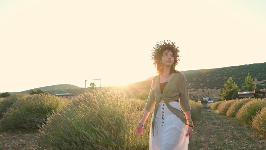 A young woman wearing a flower crown walks through a lavender garden; sunset light, mountain scenery and a rural setting create a romantic, peaceful and aesthetic summer scene. Peaceful summer mood.