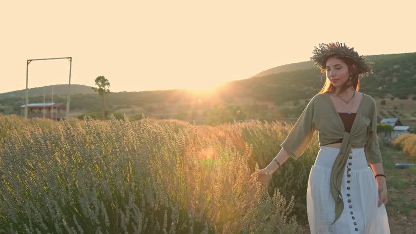 A young woman wearing a flower crown walks through a lavender garden; sunset light, mountain scenery and a rural setting create a romantic, peaceful and aesthetic summer scene. Peaceful summer mood.
