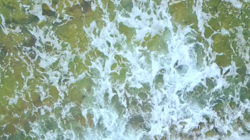 This aerial view captures the dynamic interaction of waves with the rocky coastline, highlighting the natural beauty of the seaside landscape.