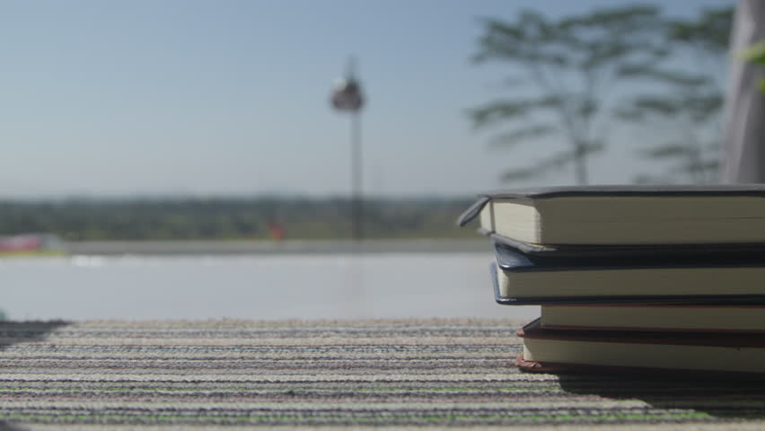 A hand place a cup of black coffee beside a neat stack of books on a carpet bathed in morning sunlight, creating a calm reading and relaxation scene at home
