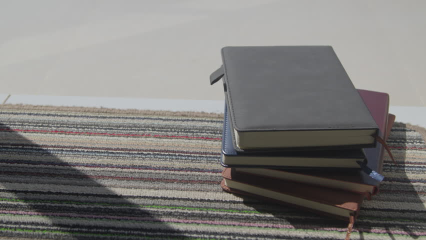 Close-up of hands placing a cup of black coffee next to stacked books on a sunlit carpet, capturing a cozy morning reading and relaxation moment indoors