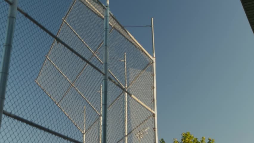 Camera pans down past a chain link fence toward bleachers and a field.