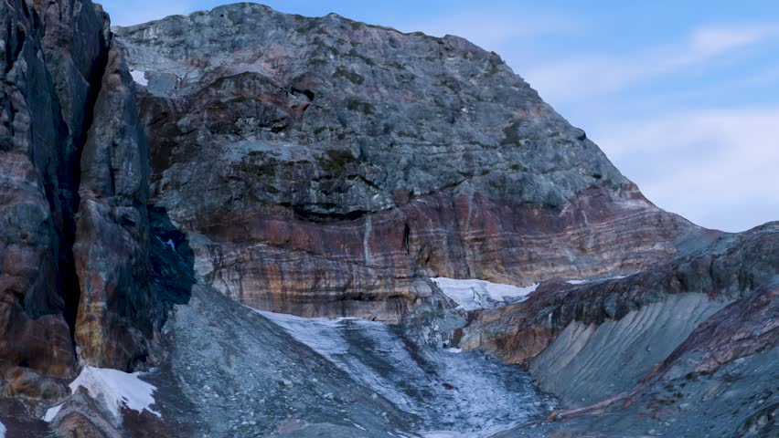 Rugged mountain peak with sedimentary rock layers, majestic alpine cliff under blue sky, cinematic rocky mountain landscape with geological textures