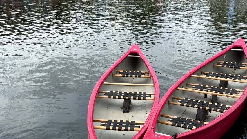 Three red canoes gently floating on calm lake water near a marina during a beautiful summer day. Peaceful outdoor recreation scene featuring canoe rental boats, waterfront leisure, eco tourism, active lifestyle, adventure travel, and relaxing nature atmosphere.