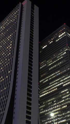SHINJUKU, TOKYO, JAPAN - JULY 2025 : Cityscape of Tokyo at night, featuring a vibrant business district and towering office buildings. A dynamic and modern urban metropolis scene. Vertical time lapse shot.