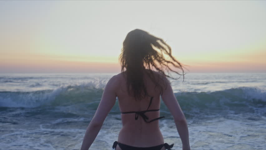 Close up of a woman walking into the ocean at Foz do Lizandro Beach in Ericeira, Portugal, with clear blue water, breaking surf and a cinematic summer lifestyle mood.