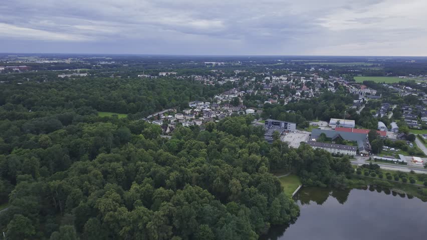 🚁🌿 Aerial drone footage of a historic manor estate surrounded by lush green parkland and a peaceful lake at sunset. Cinematic flyover showcasing heritage architecture, landscaped gardens, walking paths, and modern residential development in the background. 