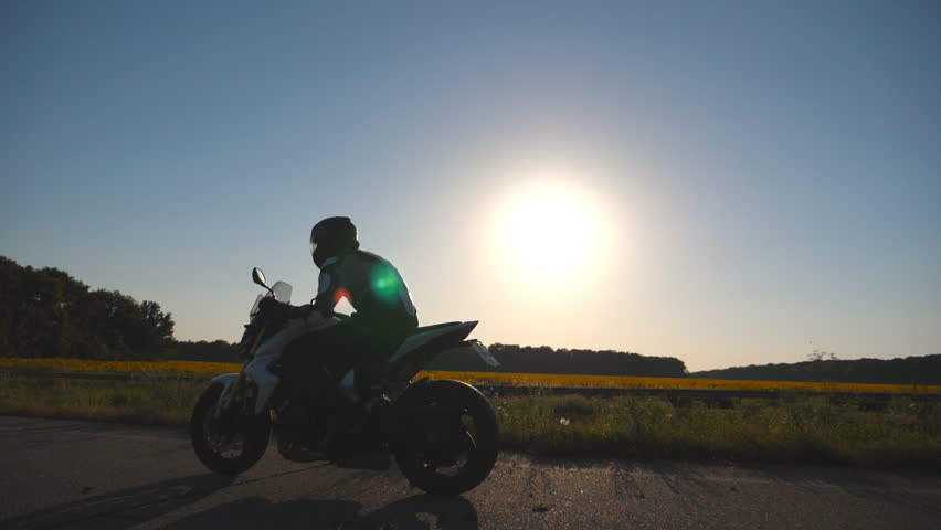 Man riding on a motorbike. Motorcyclist driving his motorcycle on country road during sunset. Slow motion Side view Close up