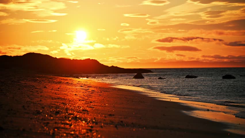 Golden hour sunset over a peaceful sandy beach with gentle ocean waves.
